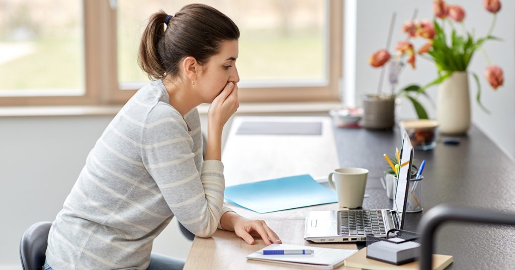 Stressad kvinna som sitter vid ett bord och tittar på en bärbar dator