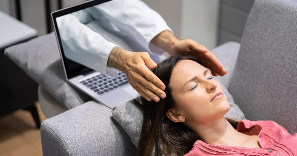 Händer som stiger fram från en laptopskärm och rör vid en kvinnas huvud