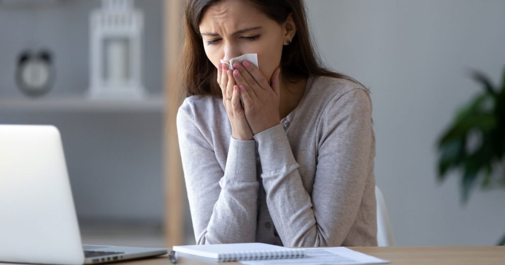 En ung kvinna snyter sig i en näsduk med slutna ögon
