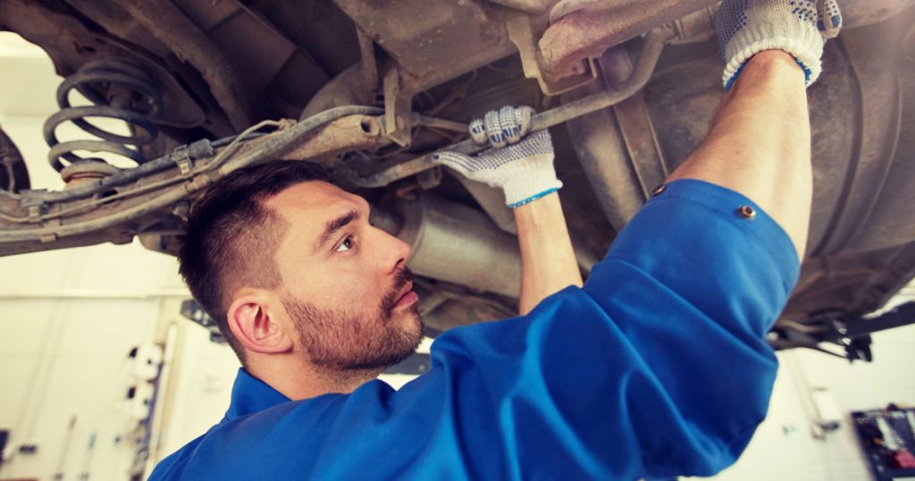 Bilmekaniker arbetar under en upplyft bil