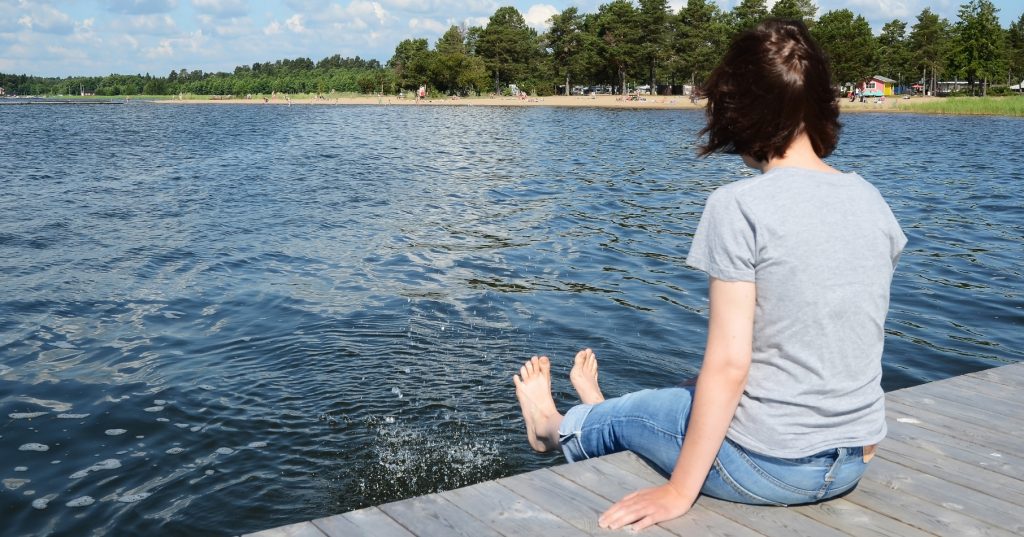 Kvinna som sitter på en brygga och doppar fötterna i vattnet