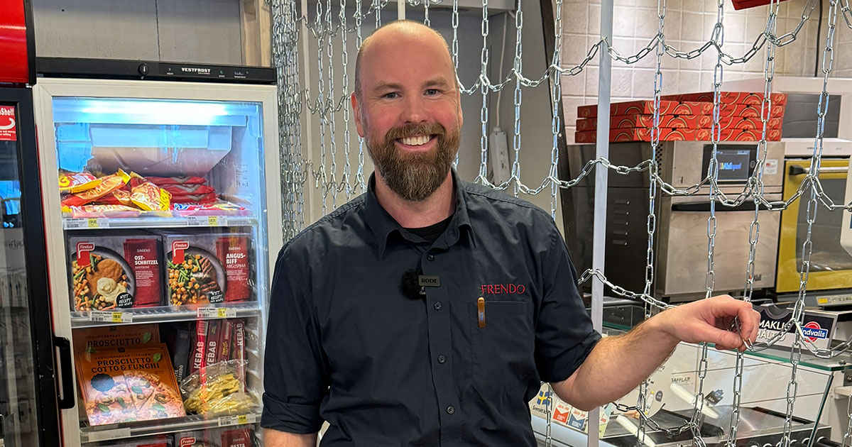 En leende skäggig man i mörk skjorta står i en livsmedelsbutik